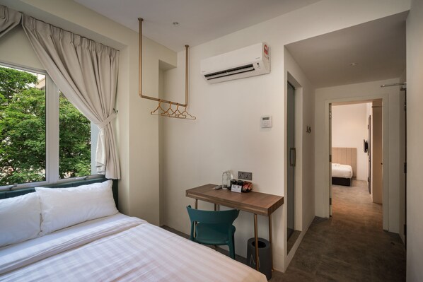 A hotel room with a bed, a desk with a chair, an air conditioning unit, and a view of trees outside. - Masson Hotel Butterworth (Seberang Jaya)