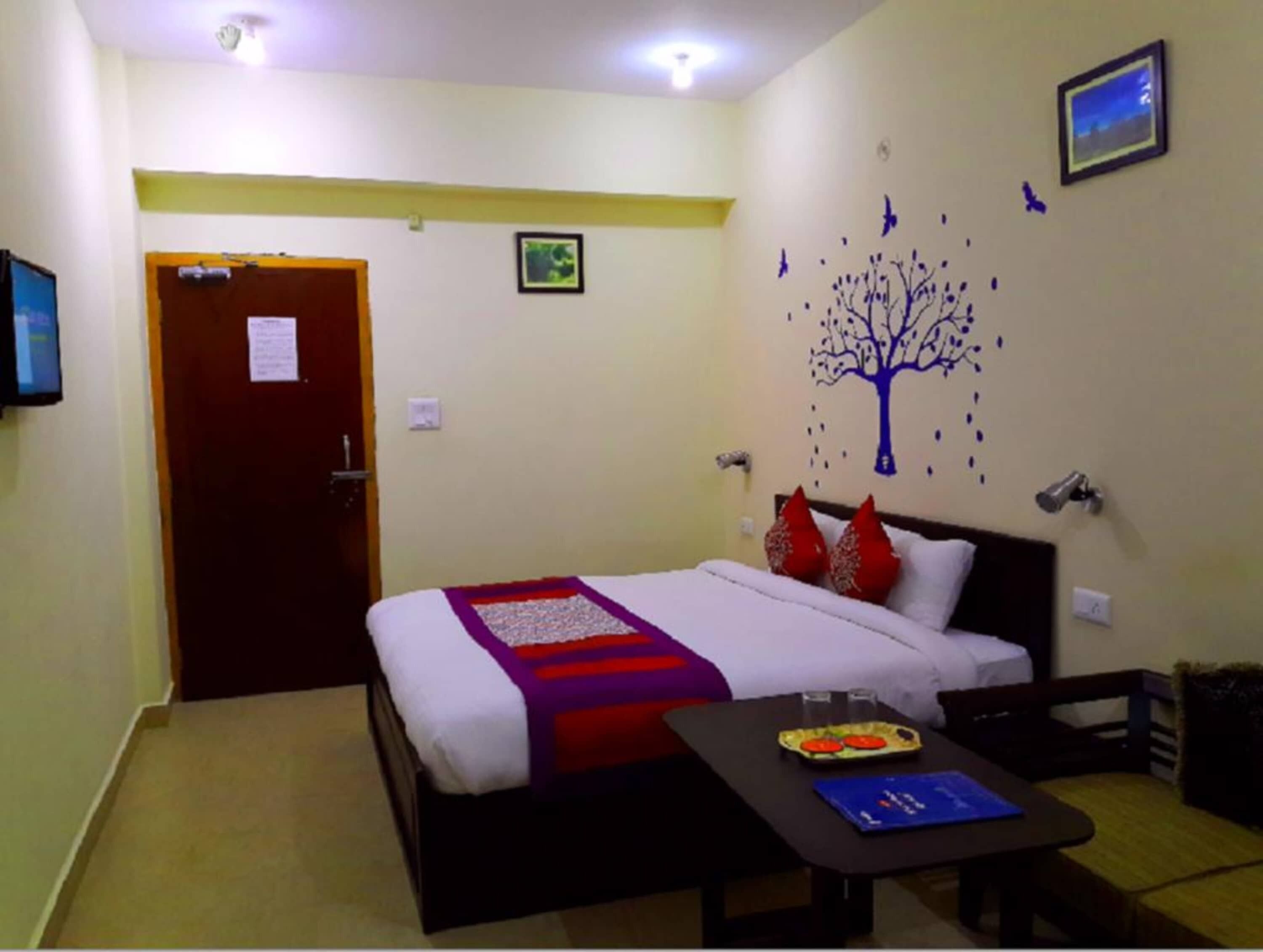 A hotel room with a bed, a small table with a tray of food, a wall-mounted TV, and a door.
