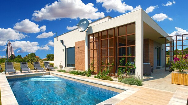 A modern building with a swimming pool, large windows, and a satellite dish.