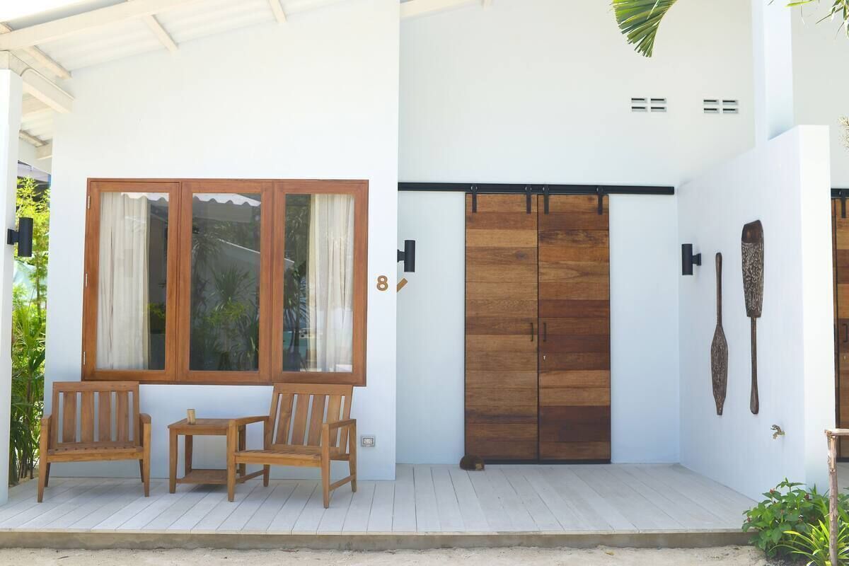 A modern house with a wooden door, a porch with two wooden chairs, and a large window with curtains.