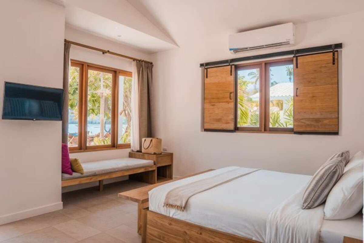 A bedroom with a bed, a window seat, a TV, and a wall-mounted air conditioner.