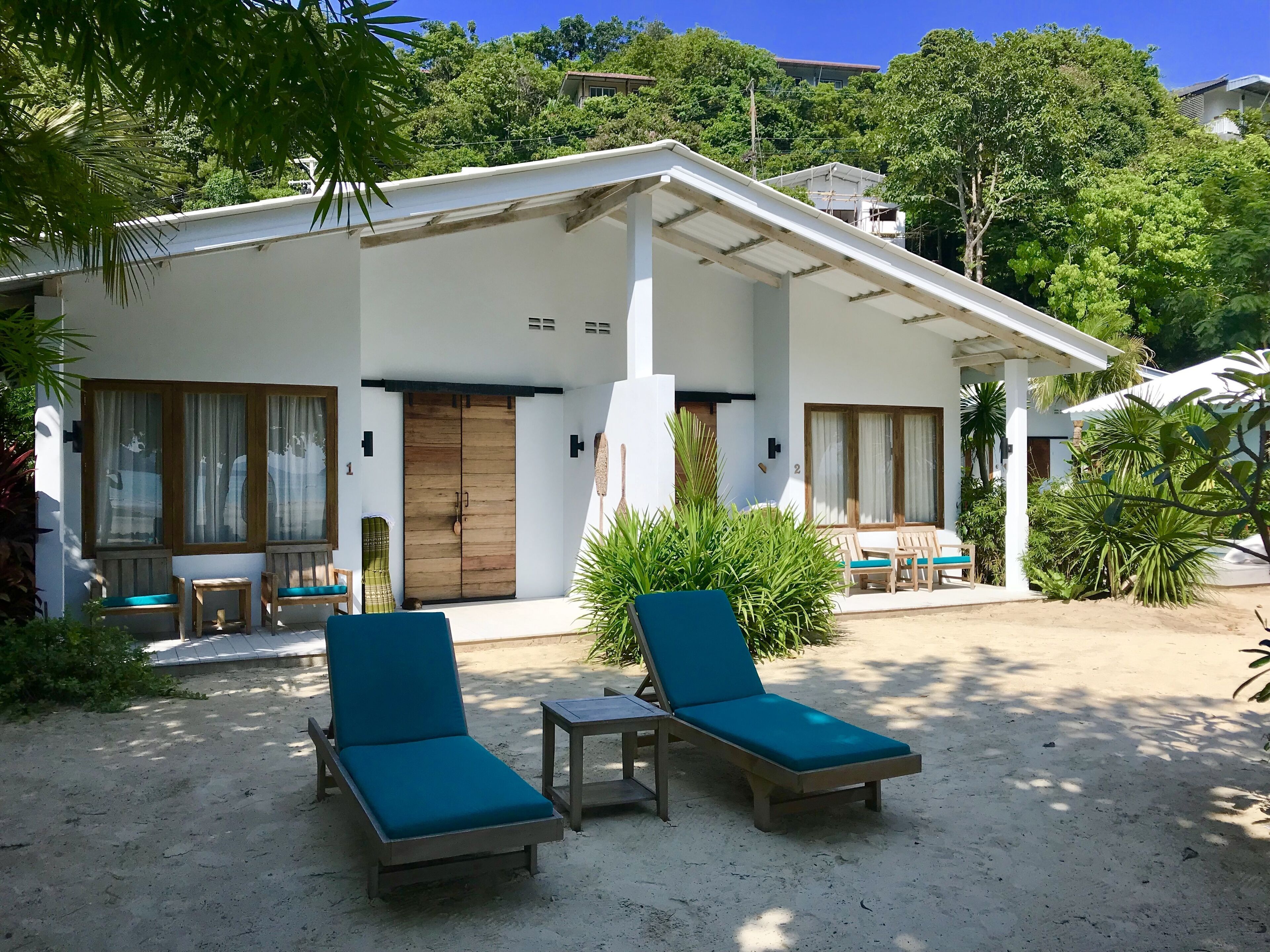 A two-story building with a covered patio, wooden doors, and a number of lounge chairs.