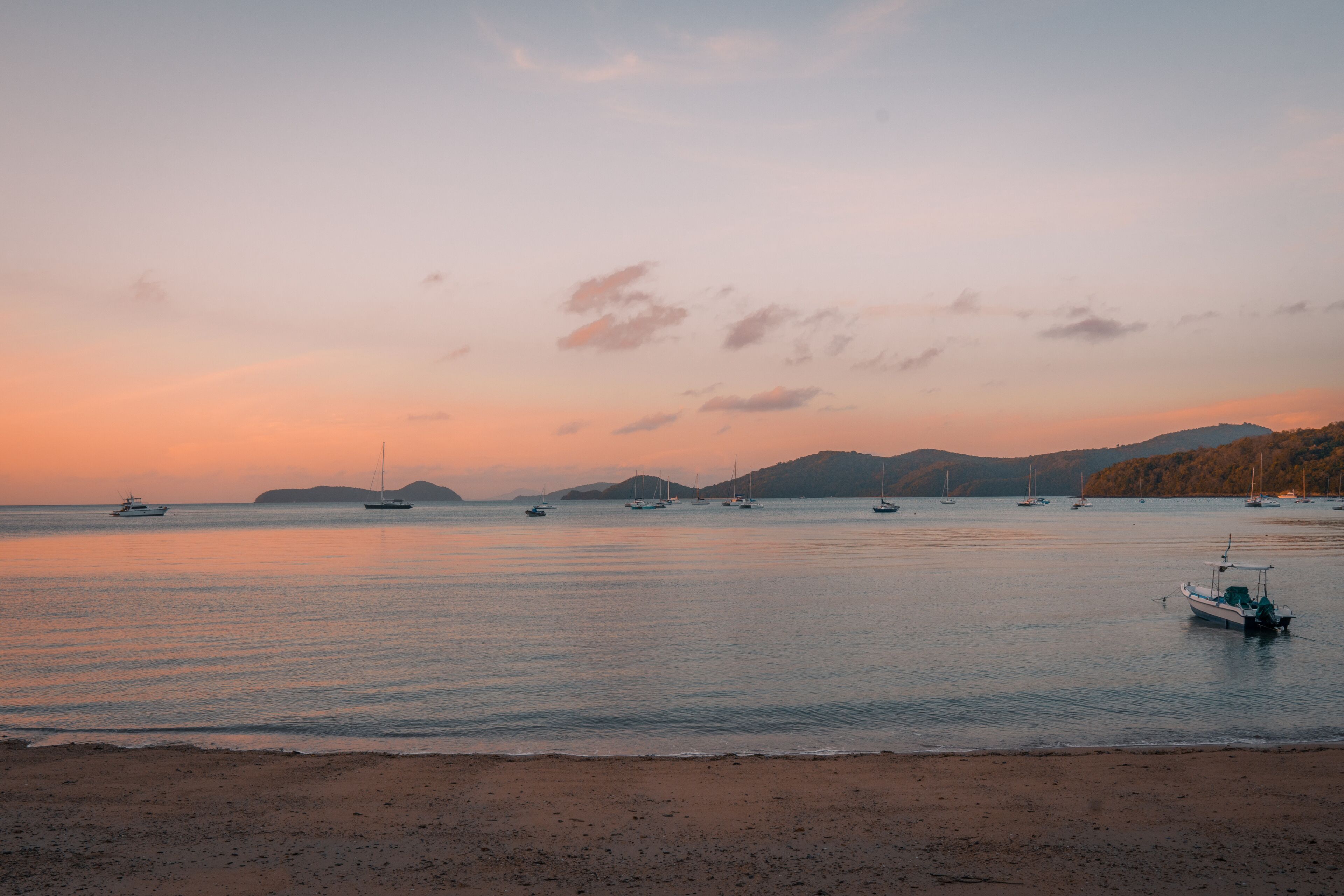 A coastal scene with calm waters, boats, and distant hills.