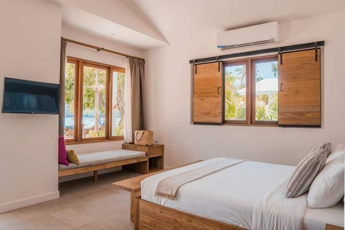 A bedroom with a bed, a window seat, a TV, and a wall-mounted air conditioner.