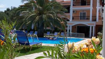 Zona de piscina con sillones de descanso, una palmera y un edificio con balcones.