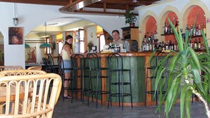 Uma área de bar com balcão, banquetes e um espaço de estar com cadeiras de vime.