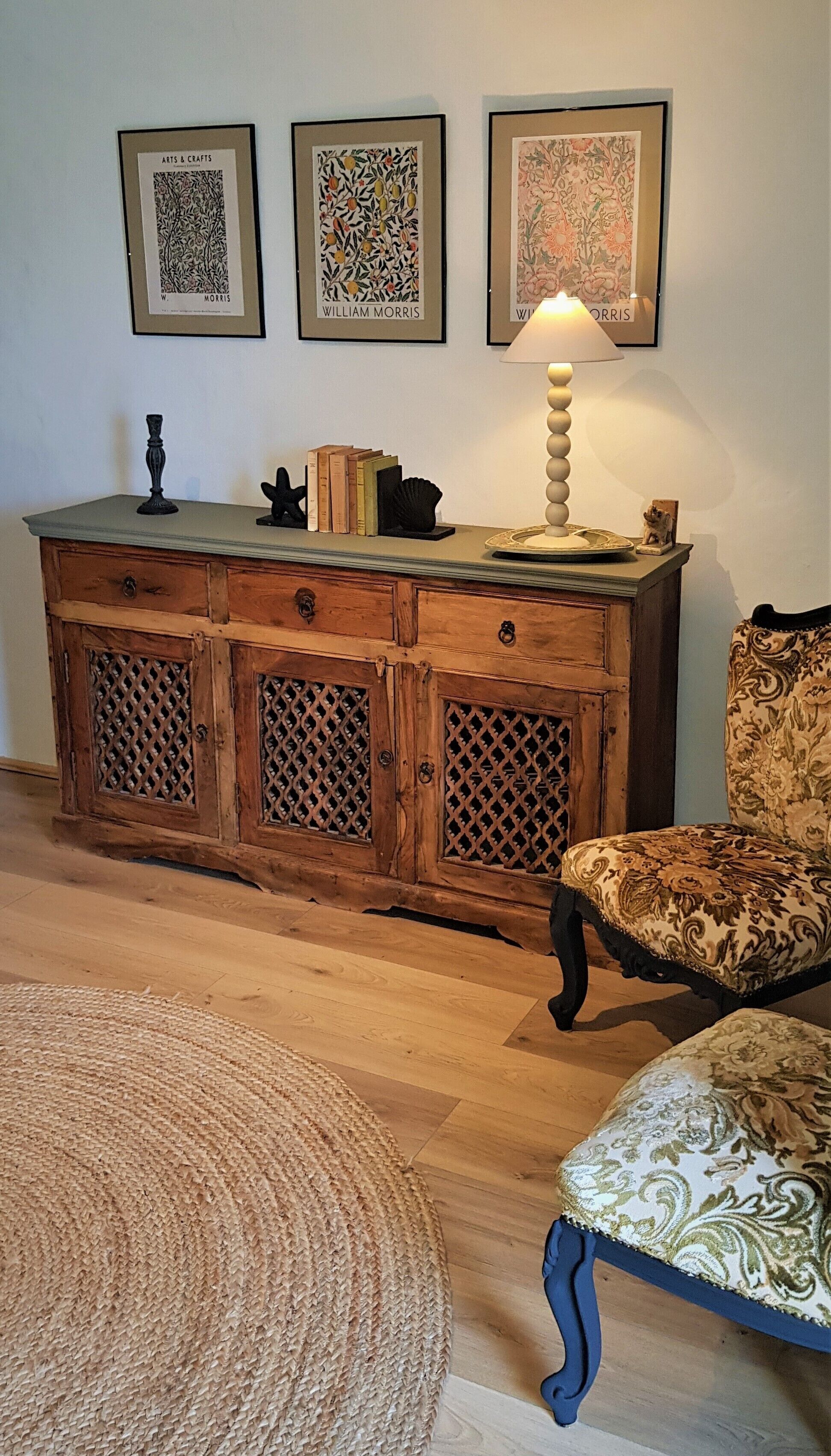 Un mueble de madera con una lámpara, una obra de arte enmarcada y una silla estampada en una habitación con suelo de madera.