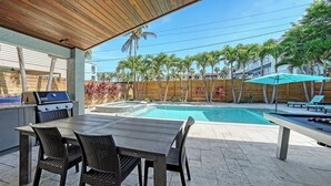 An outdoor patio with a pool, a grill, and lounge chairs.