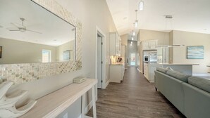 A modern kitchen with a refrigerator, a dining area with a sofa, and a hallway leading to a bathroom.