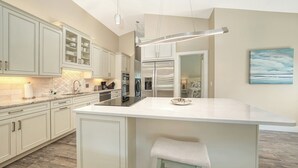 A modern kitchen with white cabinetry, a large island, and a view into the adjacent bedroom.