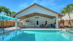 A covered outdoor area with a pool, a barbecue grill, and a table with chairs.