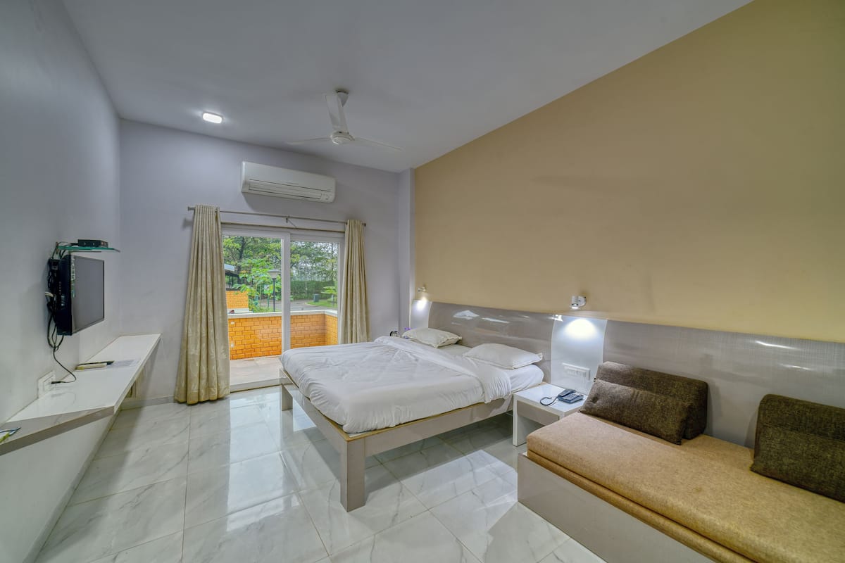 Ein Hotelzimmer mit Bett, Nachttisch, Lampe und Blick auf Grünfläche.