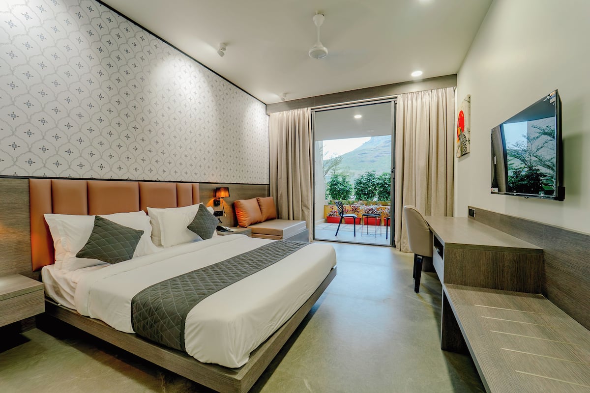 Ein modernes Hotelzimmer mit einem großen Bett, einem Schreibtisch und einem Balkon mit Blick auf Grünflächen.