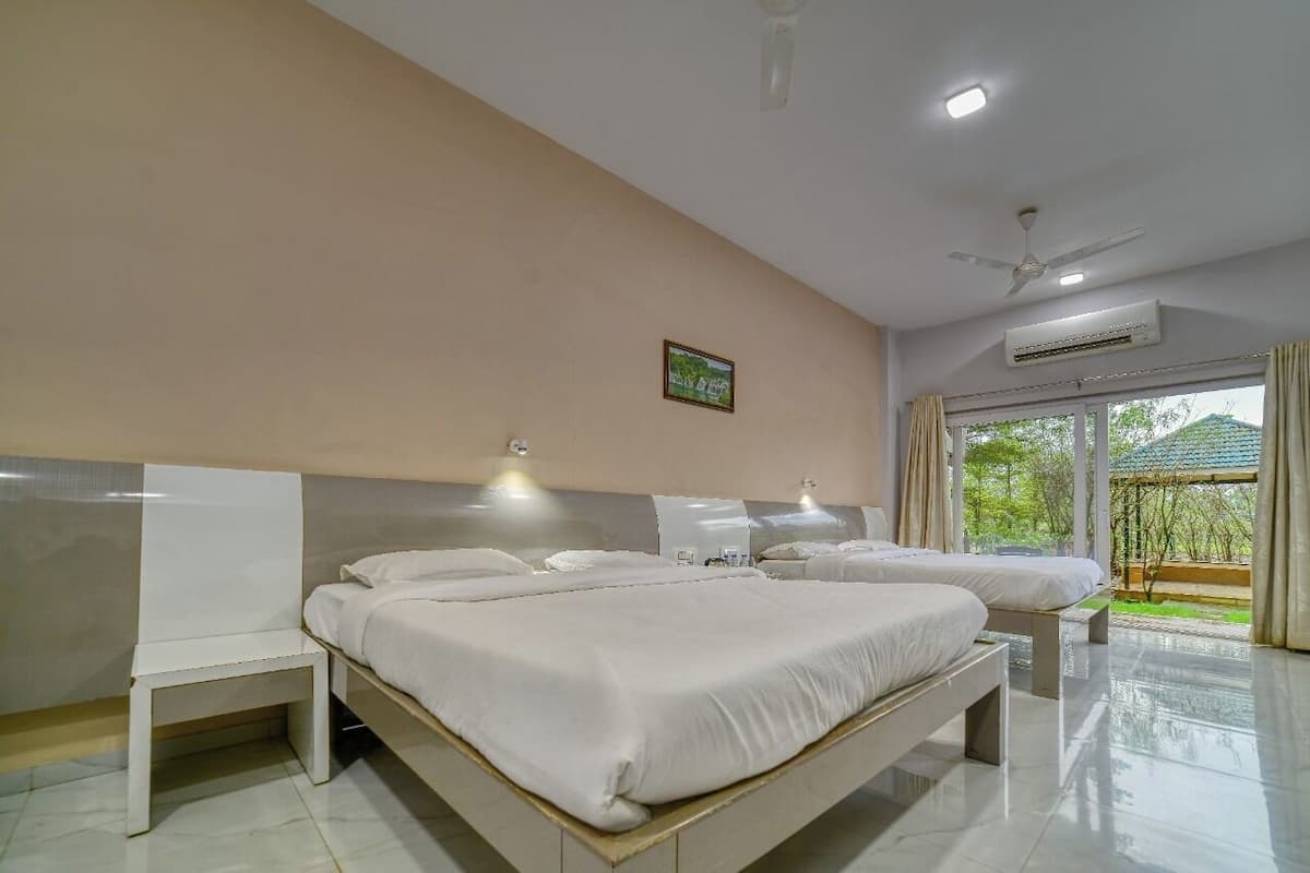 Ein Hotelzimmer mit einem großen Bett, einem Einzelbett, einem Sessel, einem Deckenventilator, einer Klimaanlage und einem fenster mit Vorhängen.