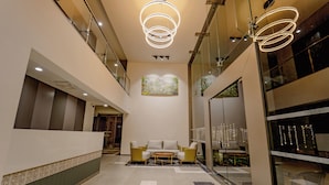 Eine großzügige Lobby mit einer Rezeption, einer Sitzecke mit Sofa und Sesseln sowie einer Glaswand mit Blick ins Freie.