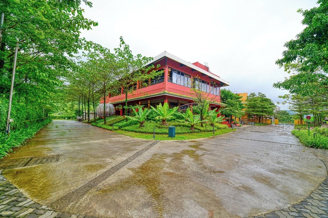 A two-story building with a red facade, surrounded by lush greenery and a paved pathway.
