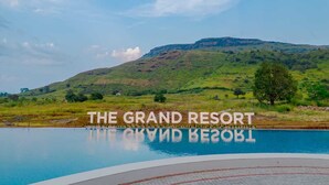 Ein Schwimmbecken mit Blick auf einen Hügel und einem Schild mit der Aufschrift 'THE GRAND RESORT'.