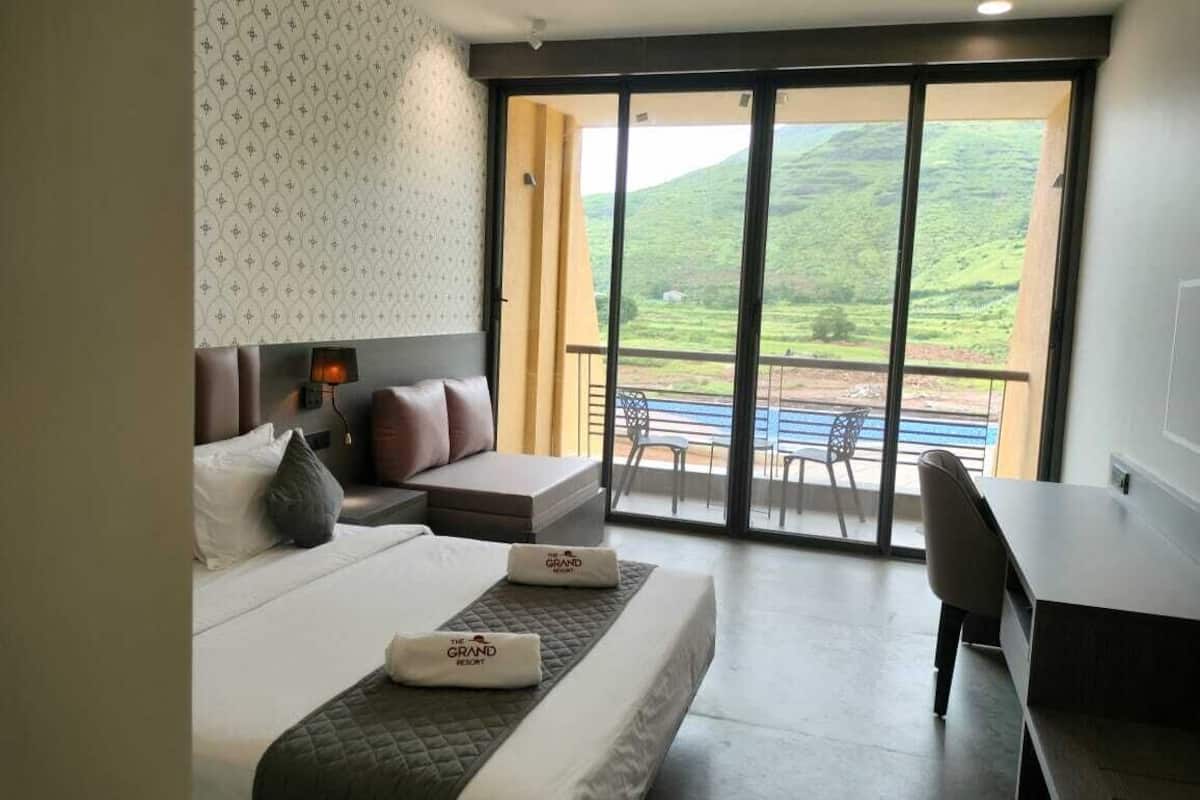Ein Hotelzimmer mit Bett, Schreibtisch und einem Balkon mit Blick auf grüne Hügel.