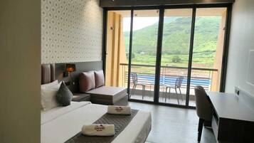 Habitación de hotel con cama, escritorio y balcón con vistas a colinas verdes.