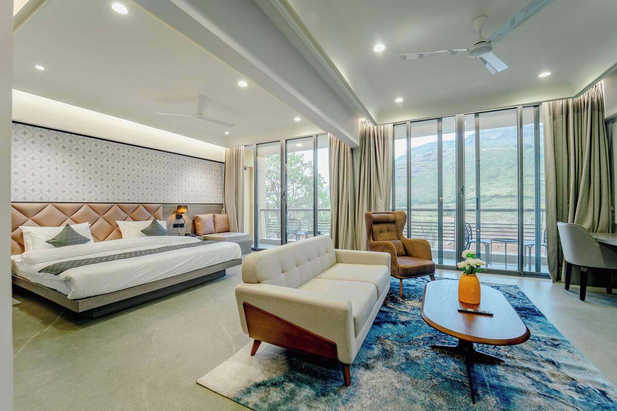Ein modernes Hotelzimmer mit einem großen Bett, einer Couch, einem Couchtisch und Blick ins Freie.