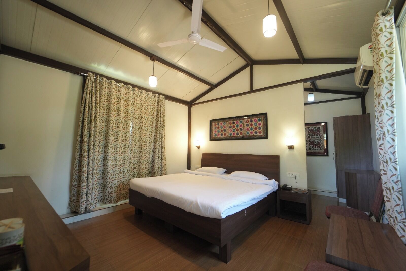 A bedroom with a large bed, a ceiling fan, patterned curtains, and a wooden floor.