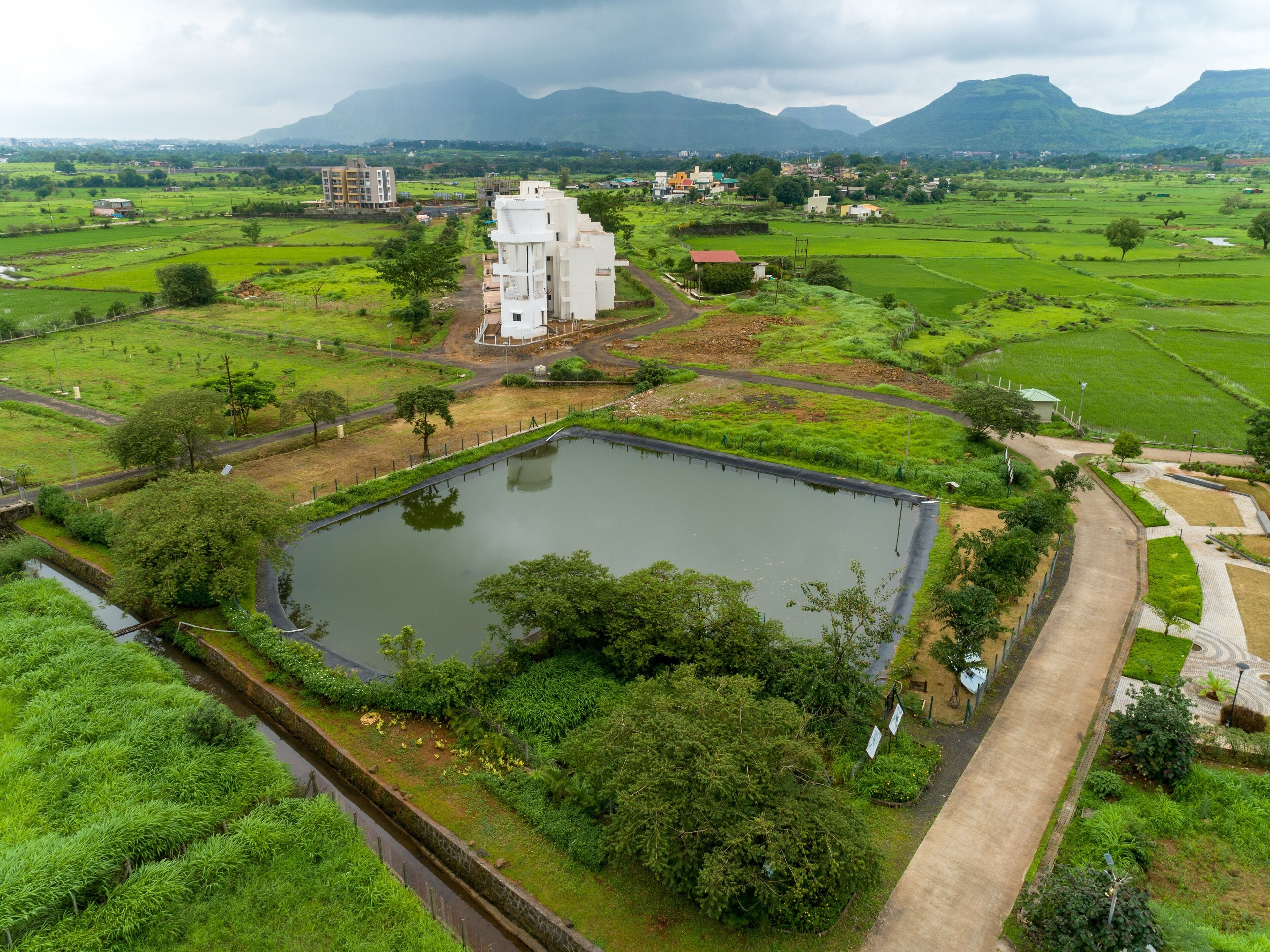 A large, rectangular water body surrounded by lush greenery and a few buildings, including a prominent white structure.