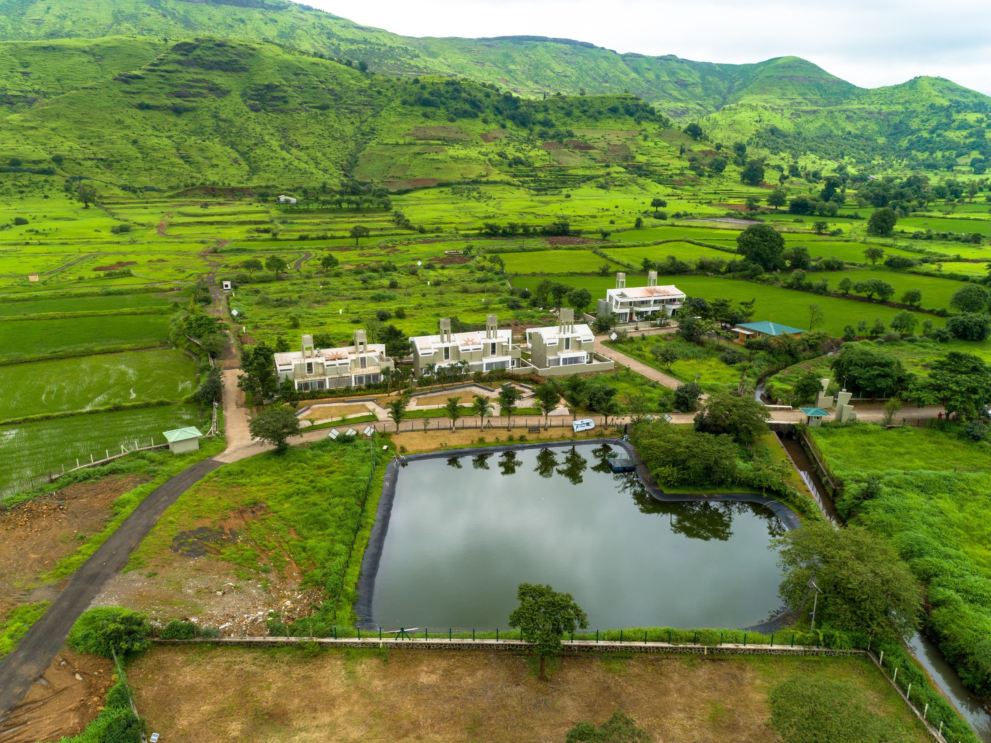 A large, modern hotel with multiple buildings, a central courtyard, and a surrounding lush green landscape with terraced fields.