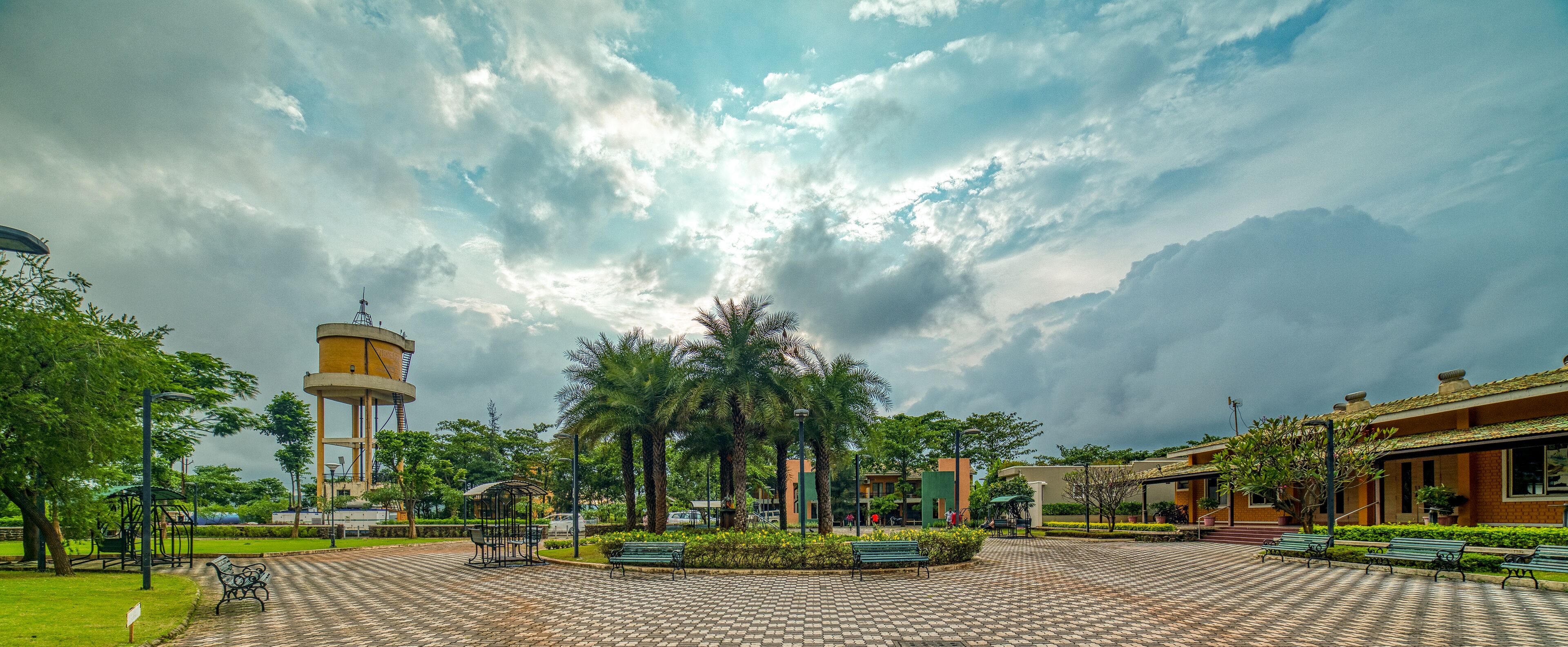 A park with a water tower, benches, and a paved walkway.