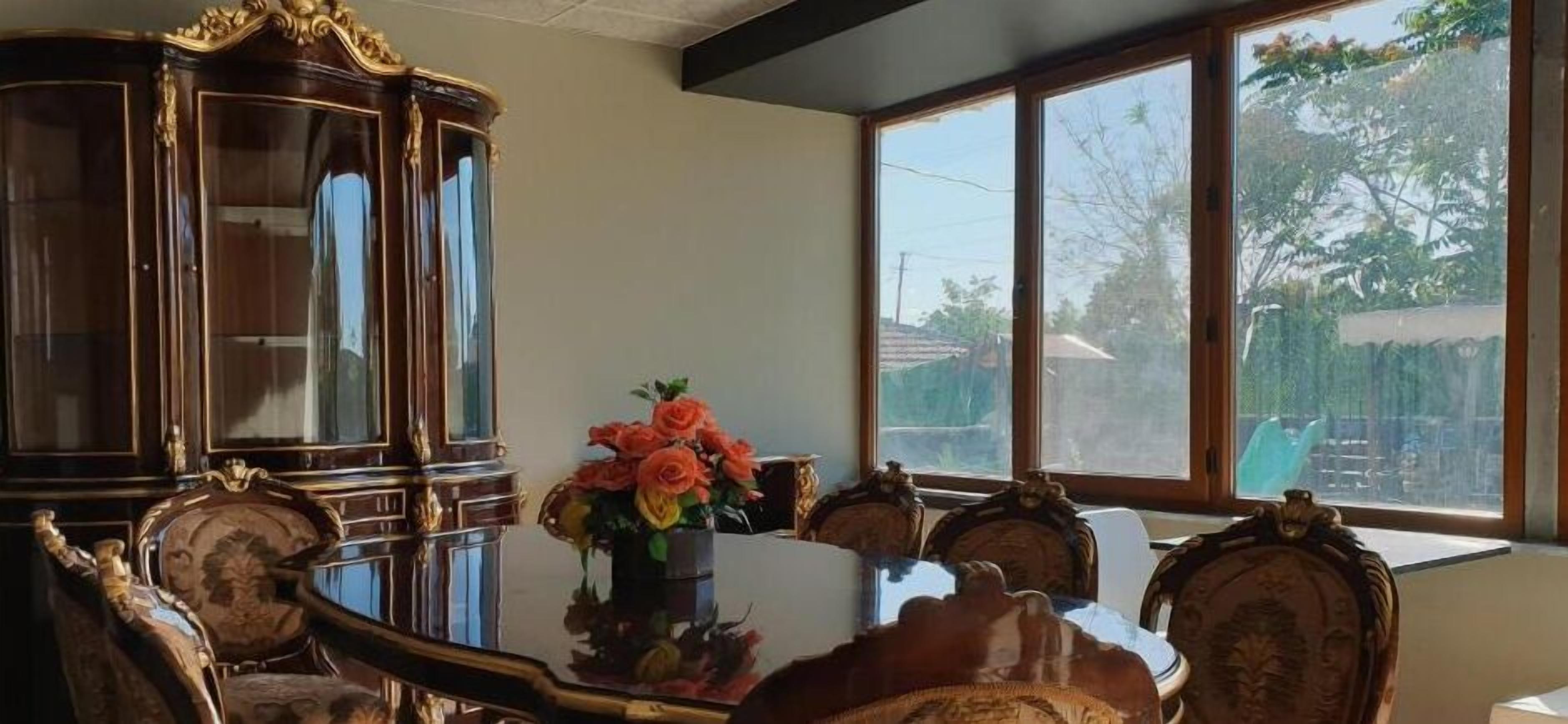 Un comedor con una mesa de vidrio, sillas ornamentadas y un aparador de madera grande.