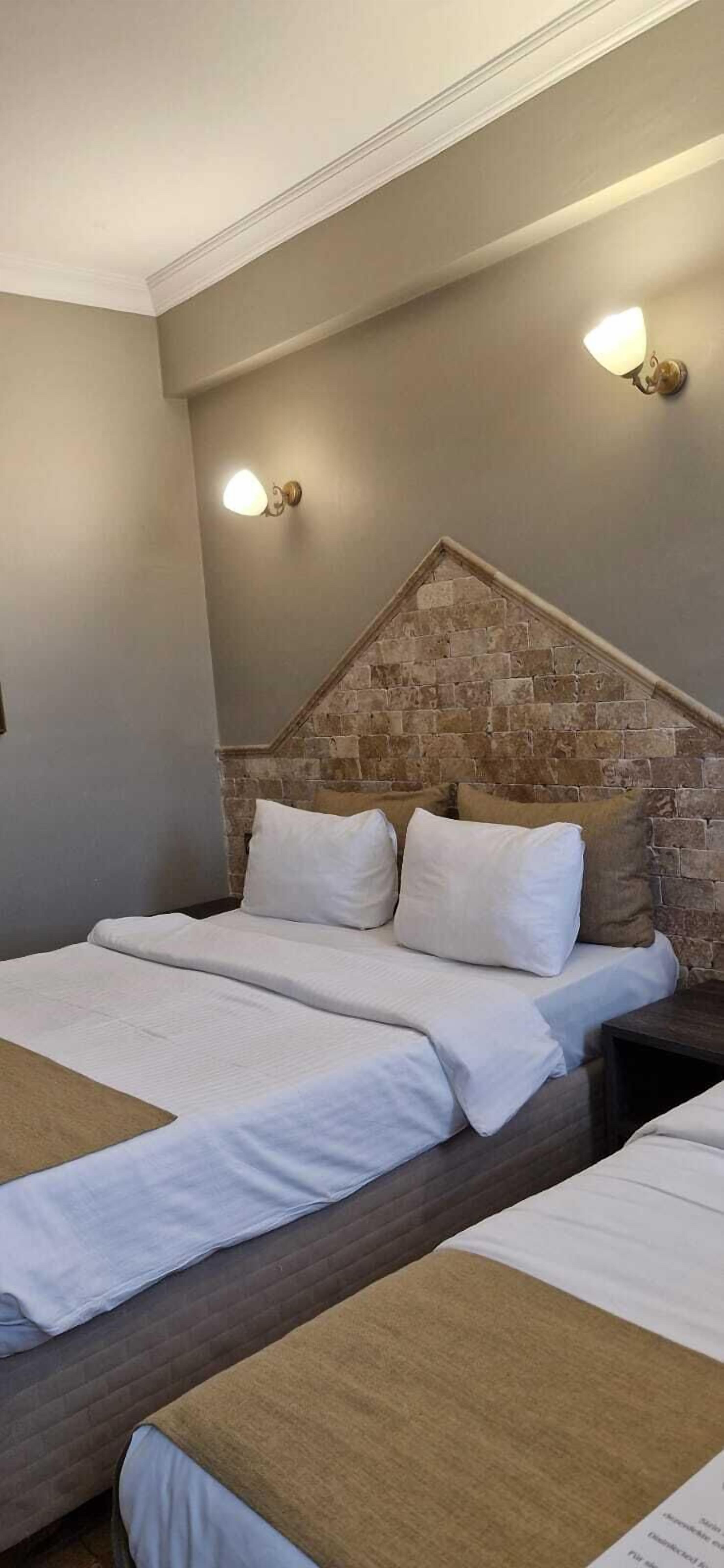 Ein Hotelzimmer mit Steinwand, einem großen Bett mit weißer Bettwäsche und zwei Wandleuchten.