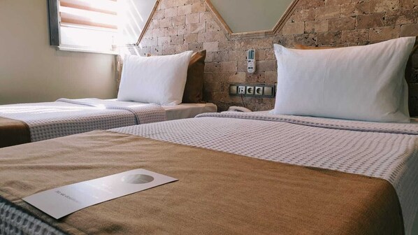 Habitación de hotel con dos camas individuales, una pared de ladrillo, una ventana con persianas y un teléfono sujeto a la pared.