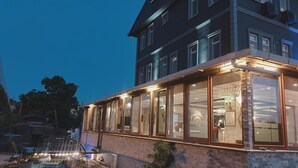 A building with a glass facade and a stone base, featuring a restaurant or cafe area with tables and chairs. - Royal Park Hotel Corlu (Corlu)