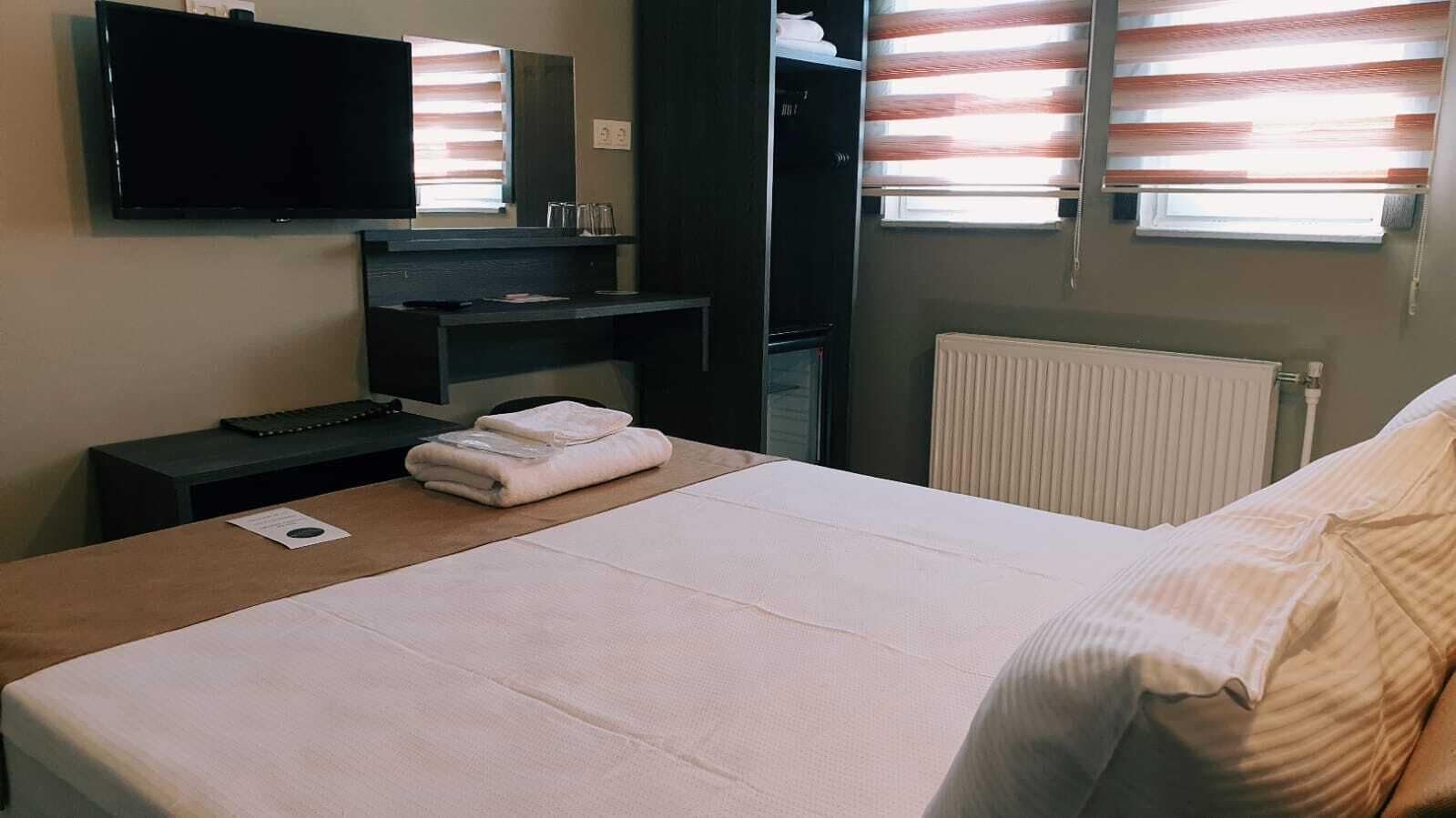 Une chambre d’hôtel équipée d’un lit, d’un bureau avec un ordinateur, d’un téléviseur à écran plat et d’une fenêtre avec des stores.