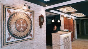 A lobby with a large mosaic wall, a reception desk, and a modern ceiling design.