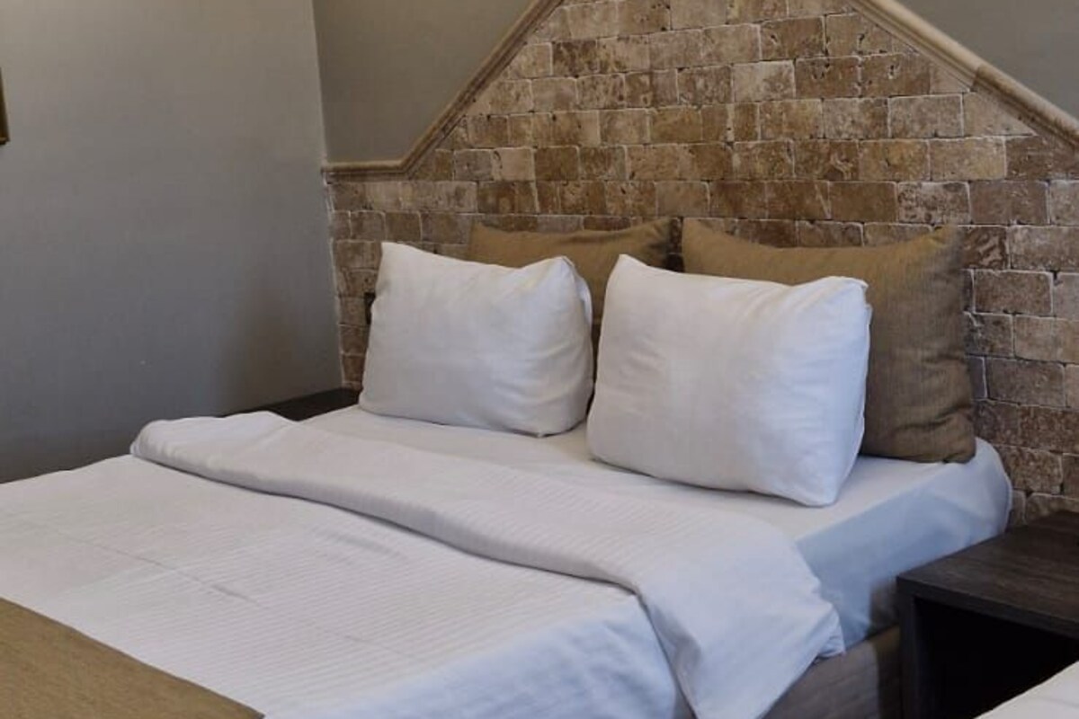 Habitación de hotel con una pared de acento de piedra, una cama grande con ropa blanca y dos lámparas de pared.
