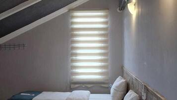 Un dormitorio con dos camas, una ventana con persianas, un calentador en la pared y una rejilla en el techo.