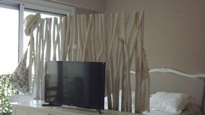 Un dormitorio con una televisión sobre un tocador, una cama con almohada blanca y cortinas.