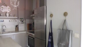 Una cocina moderna con electrodomésticos de acero inoxidable, horno empotrado y refrigerador. Hay repisas con utensilios de cocina y un bolso colgante.