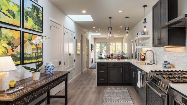 A modern kitchen with dark cabinetry, a central island, stainless steel appliances, and a skylight.