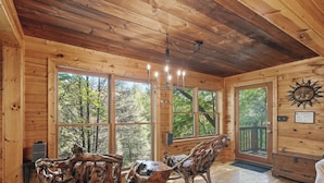 A wooden cabin interior with large windows, a chandelier, rustic wooden chairs, and a sun decoration on the wall. - Riverside Nest | No Pet Fees | Sleeps 2 | Adults Only | River front (Ellijay)