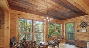 A wooden cabin interior with large windows, a chandelier, rustic wooden chairs, and a sun decoration on the wall. - Couple's Retreat, Secluded, HOT TUB,  River, Dog Friendly/fence, ADULT ONLY (Ellijay)