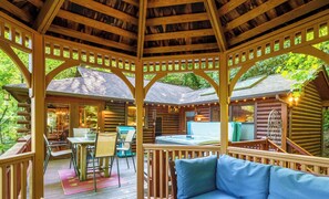 A wooden gazebo with a hot tub, a dining area, and a seating area with a blue cushion. - Couple's Retreat, Secluded, HOT TUB,  River, Dog Friendly/fence, ADULT ONLY (Ellijay)