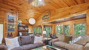 A wooden cabin interior with a sofa, a striped couch, a bookshelf, and a dining area. - Riverside Nest | No Pet Fees | Sleeps 2 | Adults Only | River front (Ellijay)