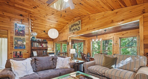 A wooden cabin interior with a sofa, a striped couch, a bookshelf, and a dining area. - Couple's Retreat, Secluded, HOT TUB,  River, Dog Friendly/fence, ADULT ONLY (Ellijay)