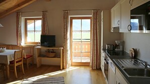 Une cuisine chaleureuse avec des poutres en bois, un coin repas avec une table et des chaises, et de grandes fenêtres agrémentées de rideaux.