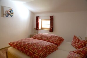 A bedroom with a bed, pillows, a window with curtains, a chair, and a wall-mounted artwork. - Valentin Vacation Apartment: 71 m², sleeps 4, 2 bedrooms (Flintsbach am Inn)