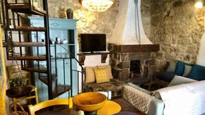 A cozy room with a stone fireplace, a wooden dining table with chairs, a blue cabinet, and a TV mounted on the wall. - Pomegranate Cottage (Giarratana)