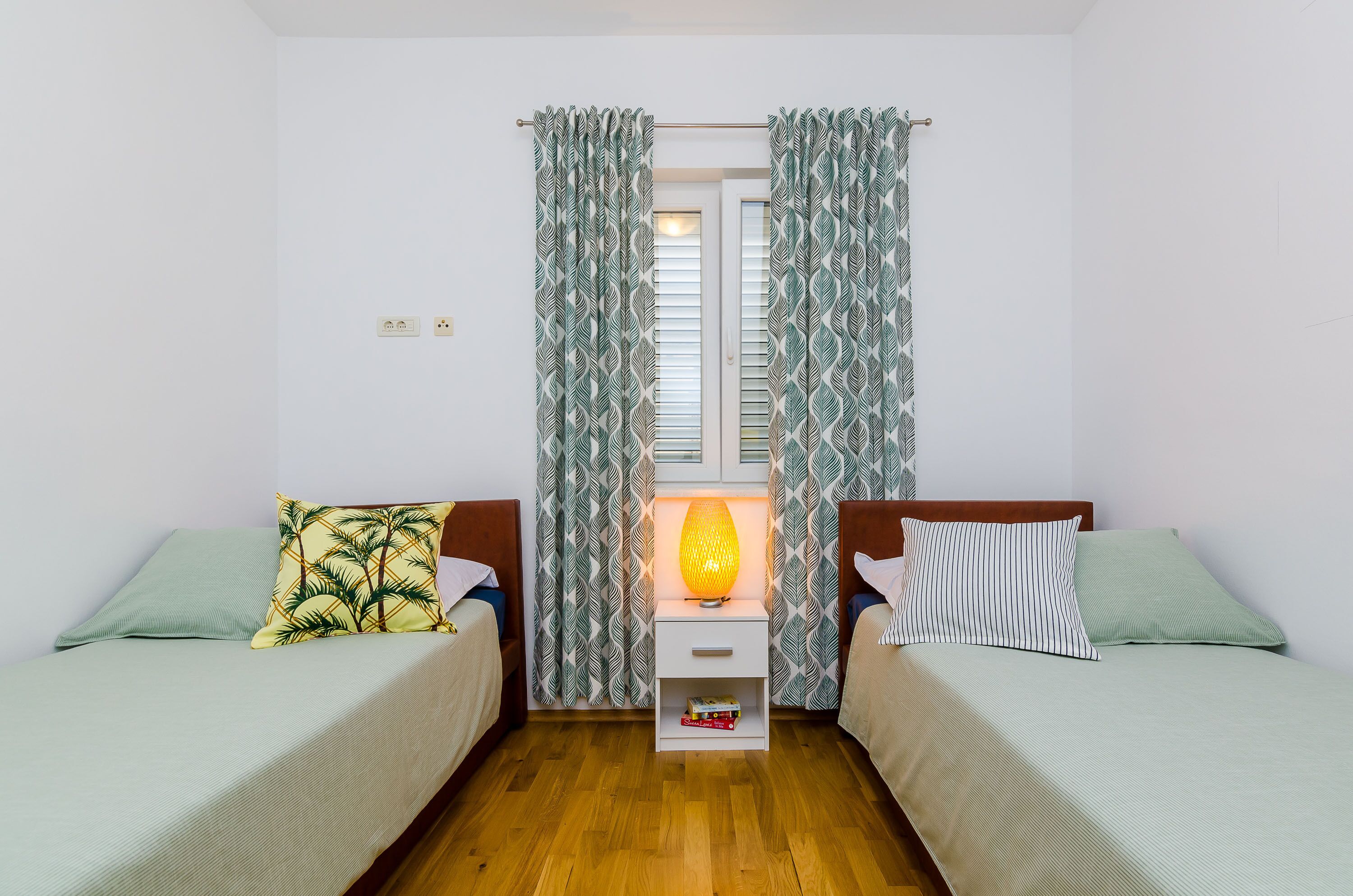A room with two beds, a nightstand with a lamp, and patterned curtains.