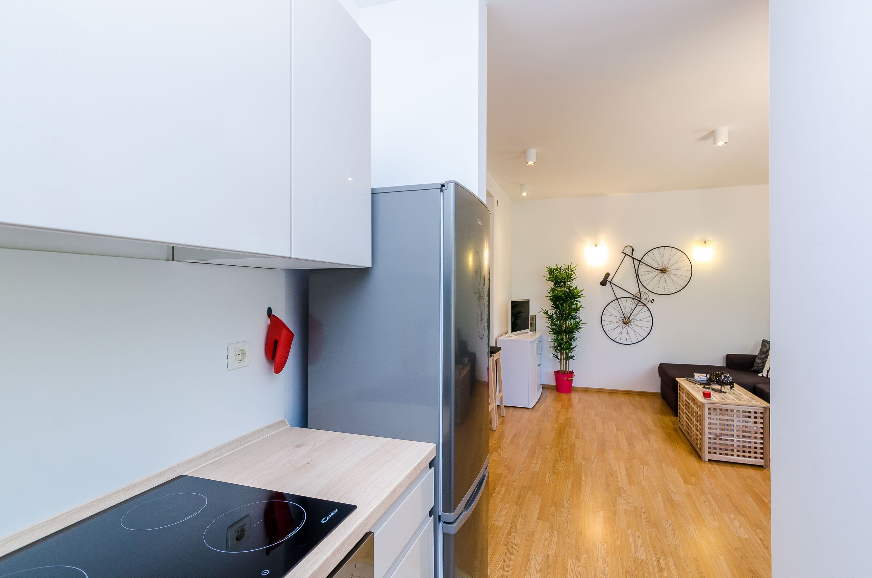 A modern kitchen with a built-in stove, a refrigerator, and a dining area with a wooden floor and a small table.