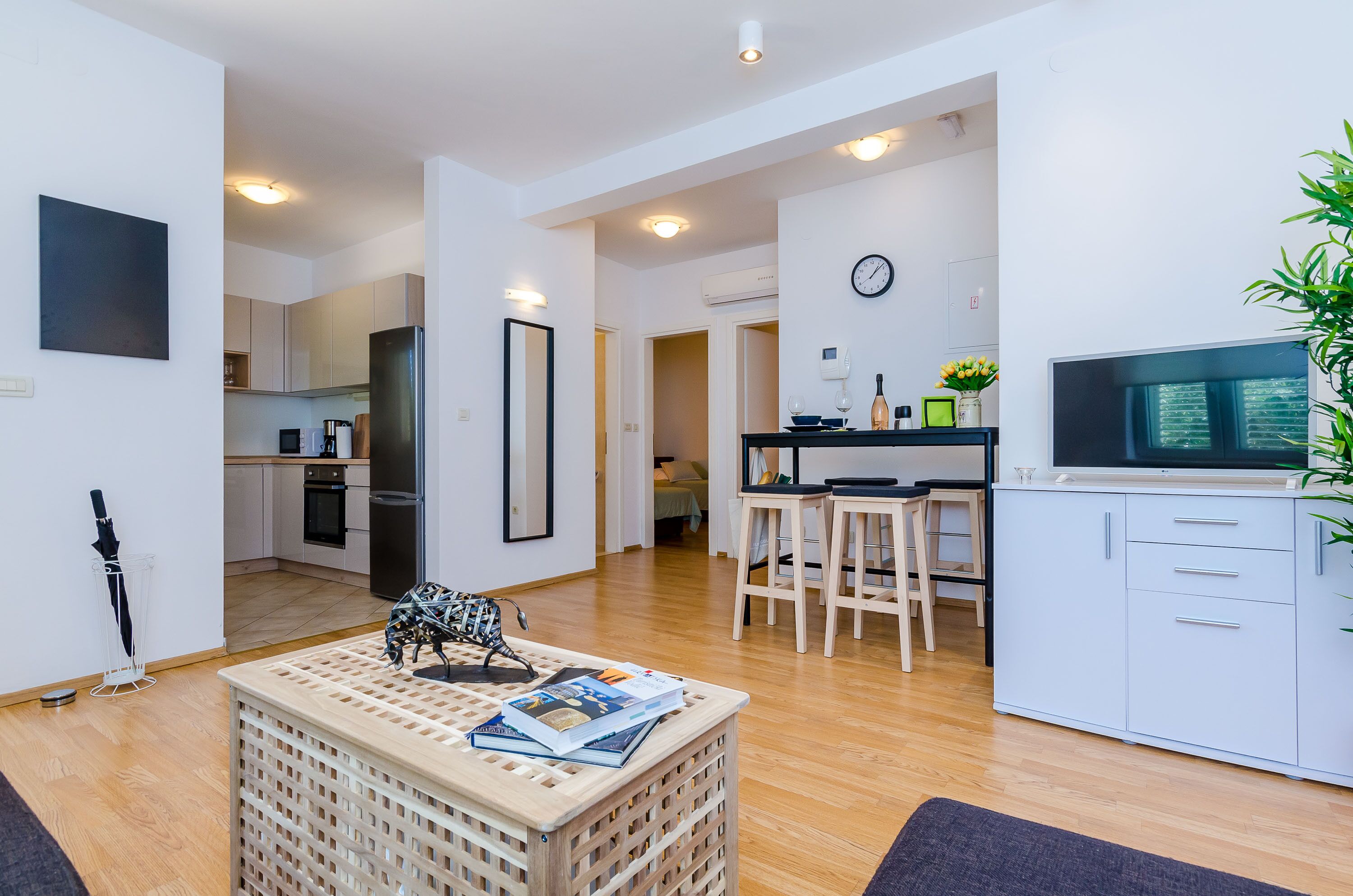 Un apartament modern amb cuina, zona de menjador i saló. Inclou televisió, taula de dinar i sofà.